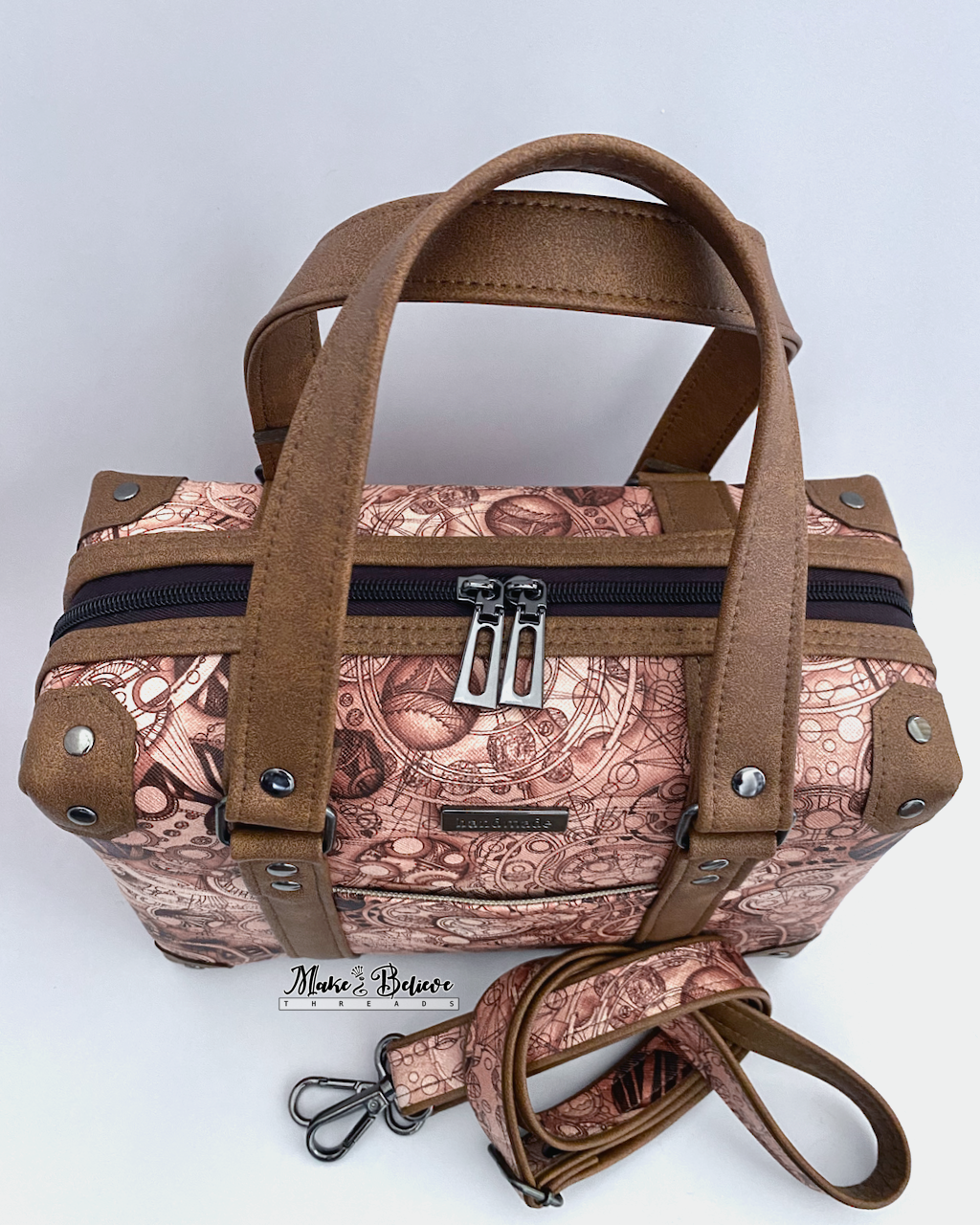 View from above of the brown handles and gunmetal hardware of a steam-trunk shaped handbag on a light gray background