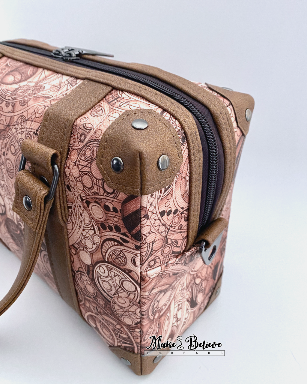 Steam-trunk detailing of brown faux leather corners and accents on language-patterned handbag, photographed on a light gray background