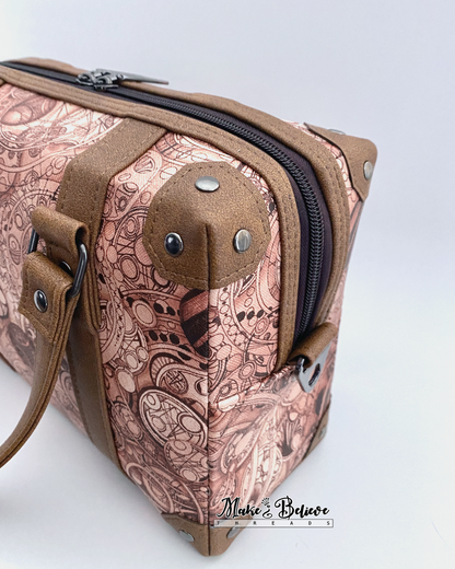 Steam-trunk detailing of brown faux leather corners and accents on language-patterned handbag, photographed on a light gray background