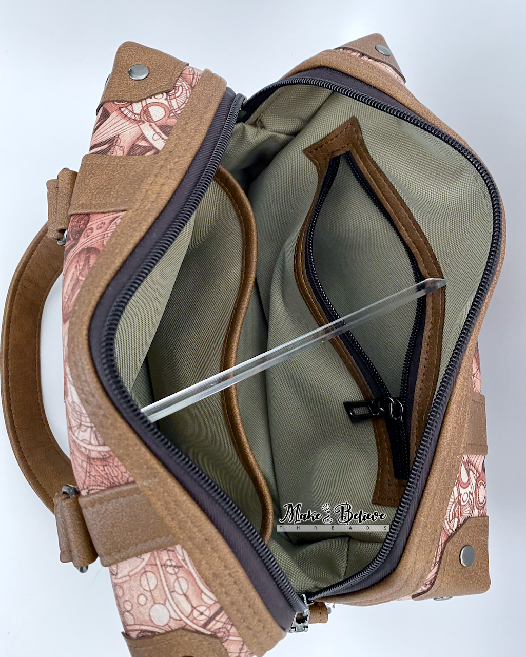 Khaki interior of steam-trunk  handbag showing zipper pocket and slip pocket with brown faux leather accents, photographed on a light gray background