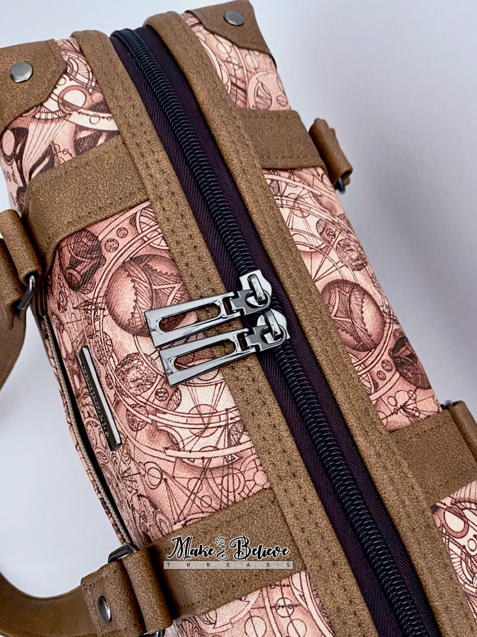 Close-up of steam-trunk and language-pattern detailing of brown faux leather handbag, photographed on a light gray background