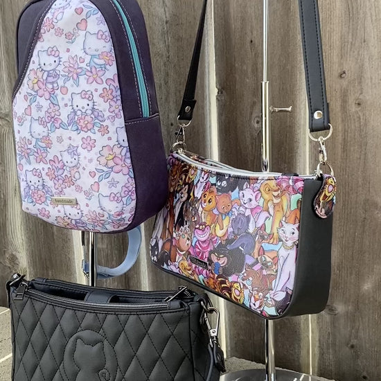 Video of three cat-themed bags in front of a wooden fence. Two are shoulder bags and one is a sling bag.