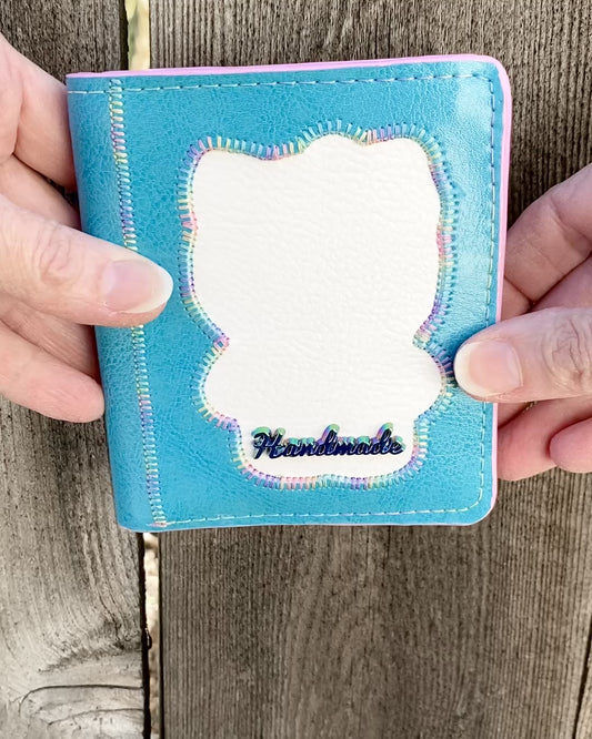 Video showing the exterior and interior of a "Bow Kitty" mini wallet with one ID window, 4 card slots, a cash slot, and two interior pockets, closed with a fashion snap. The wallet is aqua blue with a white HK silhouette reverse appliquéd in the center. Stitching is done in a pastel variegated thread and a rainbow coloured metal bag tag appears on the front.