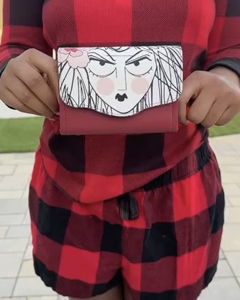 Video of person wearing a red and black checkered showing the interior details of a mini Necessary Clutch Wallet with a drawn face of a woman, print from Alexander Henry's Ghastlies collection